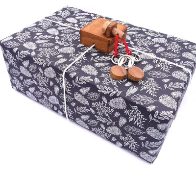 Geschenkbox mit KEEPR Fort Knox Rätselbox auf dunkel gemustertem Papier, verschnürt, Holzpuzzle liegt obenauf.