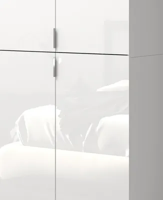 A close-up view of a white high-gloss wardrobe with silver handles, reflecting soft light and furniture.