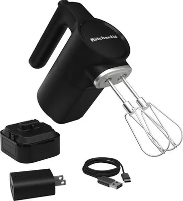 A black KitchenAid cordless hand mixer with its accessories, including a battery pack, USB charging cable, and wall adapter, is displayed against a white background.
