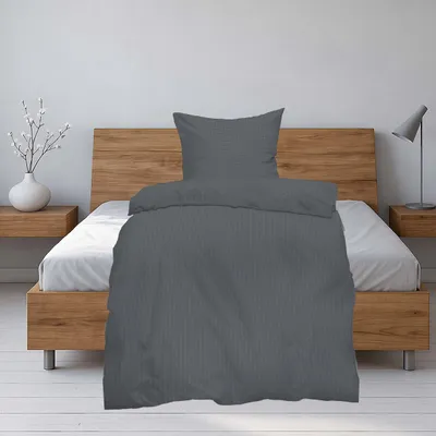 A bed with grey seersucker bedding and a pillow.