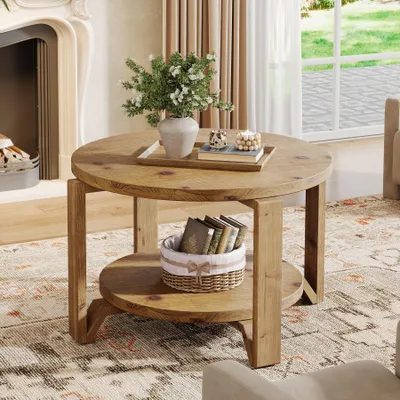 A round wooden coffee table with two shelves, decorated with a vase of flowers and books, in a living room setting.