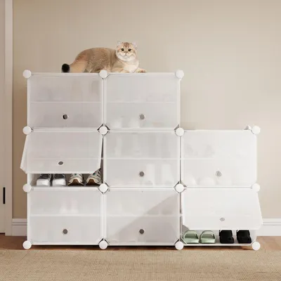 A cat is resting on top of a white modular shoe rack filled with shoes.