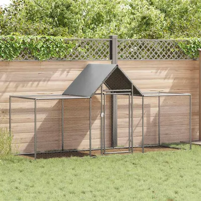 A chicken coop is set up in a grassy backyard with a wooden fence and green foliage in the background.