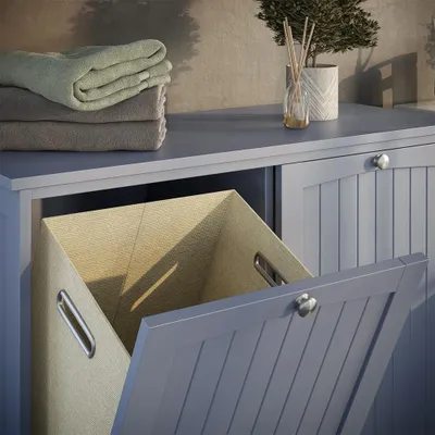 A close-up view of a grey laundry cabinet with a laundry basket inside and towels stacked on top.