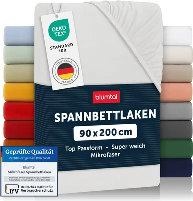 A stack of folded fitted sheets in various colors, with a white fitted sheet prominently displayed in the foreground, featuring product information tags.