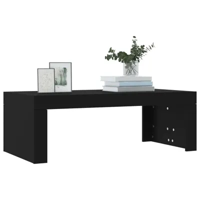 A black coffee table with two framed pictures and a vase of greenery on top, set against a white background.