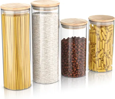 Four glass storage jars with bamboo lids, containing spaghetti, rice, coffee beans, and penne pasta.