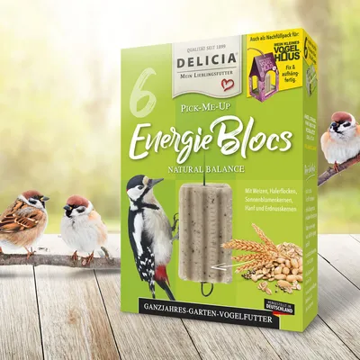 A product box for bird food is displayed with birds perched on a branch in front of it, set against a blurred natural background.
