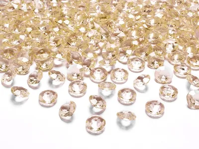 A pile of small, faceted, gold-colored confetti pieces, resembling diamonds, scattered on a white surface.