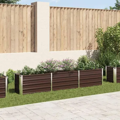 A row of brown metal raised garden beds filled with plants, set against a wooden fence and a light-colored wall.