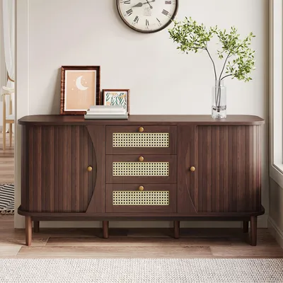 A wooden sideboard with rattan drawer fronts and doors, decorated with framed pictures and a vase of greenery, placed in a room.