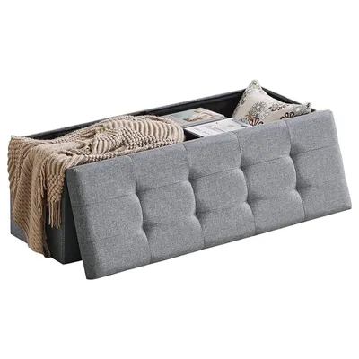 An open storage ottoman with a blanket and books inside, shown from a diagonal angle.