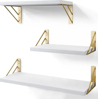 Three white shelves with gold geometric brackets mounted on a white wall.