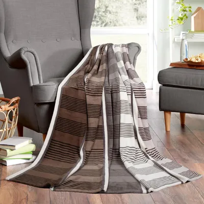 A striped blanket draped over a gray armchair next to a basket and books.