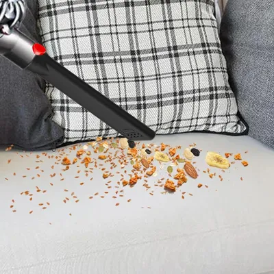 A vacuum cleaner attachment is shown cleaning up spilled granola and nuts on a white couch.