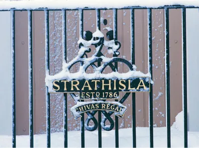 A metal gate covered in snow with a sign that reads "STRATHISLA ESTD 1786 CHIVAS REGAL".