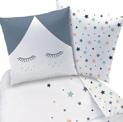 A close-up view of bedding with a star pattern and a pillow with a face design.