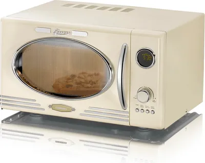 A cream-colored retro-style microwave oven is shown from a three-quarter front view, set on a reflective surface.