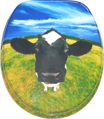 A toilet seat with a cow's head printed on it, set against a background of a green field and blue sky.
