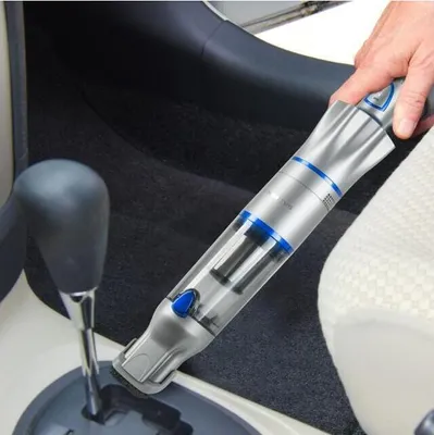 A person is cleaning the interior of a car with a handheld vacuum cleaner.