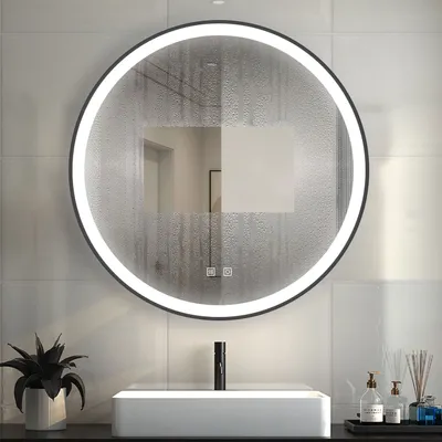 A round LED mirror with a black frame is mounted on a tiled wall above a white rectangular sink. The mirror has a frosted effect with water droplets. A black faucet is visible in the sink, and to the right, there are two bottles of soap and a diffuser with