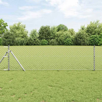 A chain-link fence in a grassy field with trees in the background.
