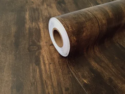 A roll of self-adhesive wood-effect film with a dark brown wood grain pattern.