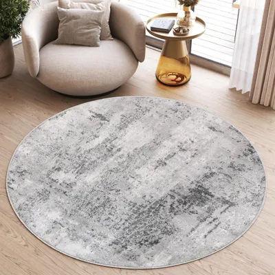A round rug with a distressed pattern is placed on a wooden floor in a living room setting, next to a modern armchair and a side table.