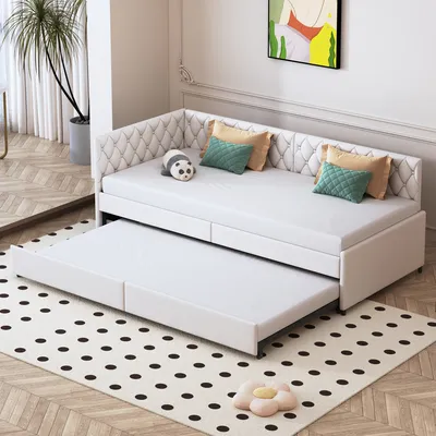 A white daybed with an extended trundle bed is shown in a room with a polka dot rug and a plant in the background.