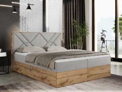 A bedroom scene featuring a large boxspring bed with a wooden base and a grey upholstered headboard.