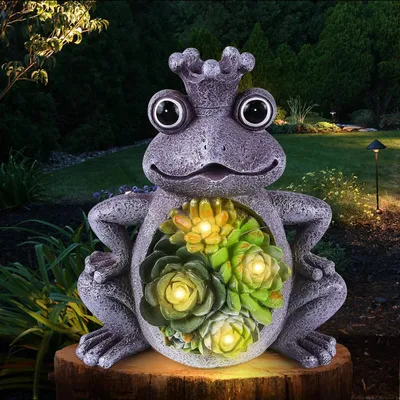 A solar-powered frog statue with succulent plants and lights, placed in a garden at night.
