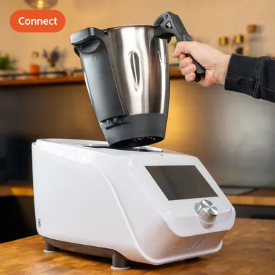 A person is holding a mixing bowl attachment over a white kitchen appliance.