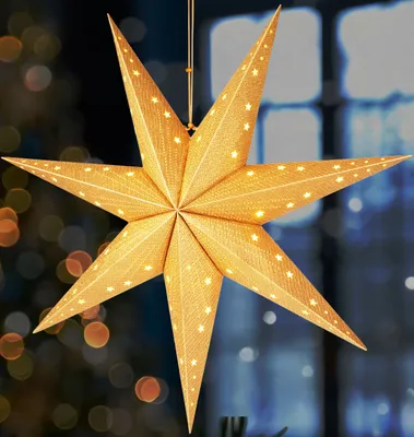 A lit paper star decoration hangs in front of a blurred background with lights.