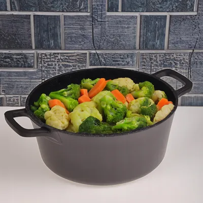 A pot filled with mixed vegetables, including broccoli, cauliflower, and carrots, sits on a white surface against a tiled background.