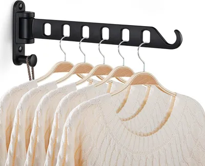 A black wall-mounted retractable clothes drying rack with several white sweaters hanging on wooden hangers.