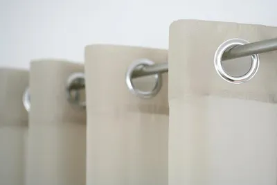 A close-up view of several eyelet curtains hanging on a metal rod against a white background.