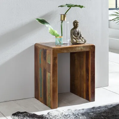 A wooden side table with decorative items on top, placed against a white wall.