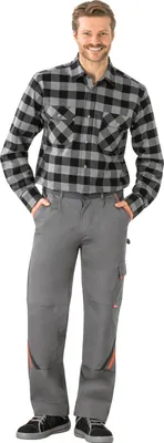 A man wearing work pants and a plaid shirt, standing against a white background.