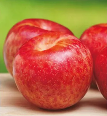 Three red plums are arranged on a wooden surface with a blurred green background.