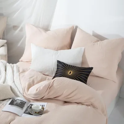 A neatly made bed with several pillows and a duvet, a book and a teacup are placed on the bed.