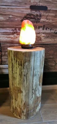 A salt lamp sits on a wooden log stand in front of a wooden plank wall.