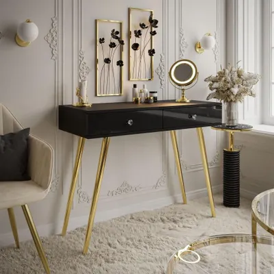 A modern vanity table with gold legs and drawers, decorated with wall art and a mirror, in a well-lit room.