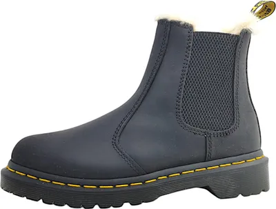 A single black Dr. Martens boot with yellow stitching and cream-colored fur lining is shown against a white background.