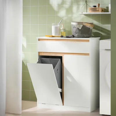 A bathroom cabinet with a laundry basket and drawer, set against a tiled wall.