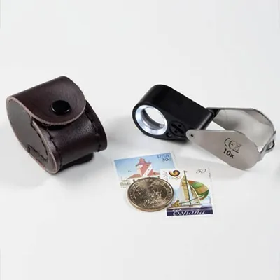 A leather case, a magnifying glass with LED light, a coin, and two stamps are arranged on a white surface.