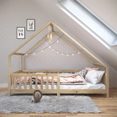 A child's bed with a house-like frame, decorated with string lights and a dreamcatcher, in a room with polka-dot wallpaper and a skylight.