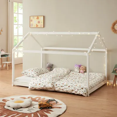 A child's bedroom with a white house-shaped bed frame decorated with fairy lights.