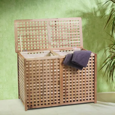 A wooden laundry hamper with a lattice design, open lid, and two purple towels draped over the side, set against a green wall.