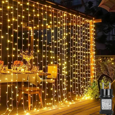 A string of warm white fairy lights hanging down over an outdoor dining area with a table set for a meal.