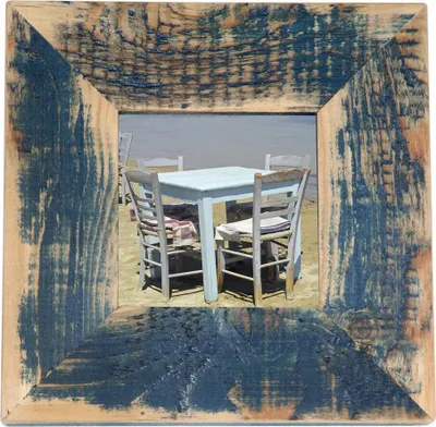 A rustic wooden picture frame with a dark blue distressed finish, showcasing a scene of an outdoor cafe with tables and chairs on a sandy beach.